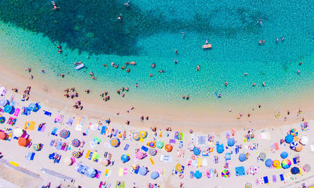 People bathing in the sun at the beach, aerial view with clear blue water and sandy beach. Corfu island Kerkyra, Greece (photo via CalinStan/iStock/Getty Images Plus)