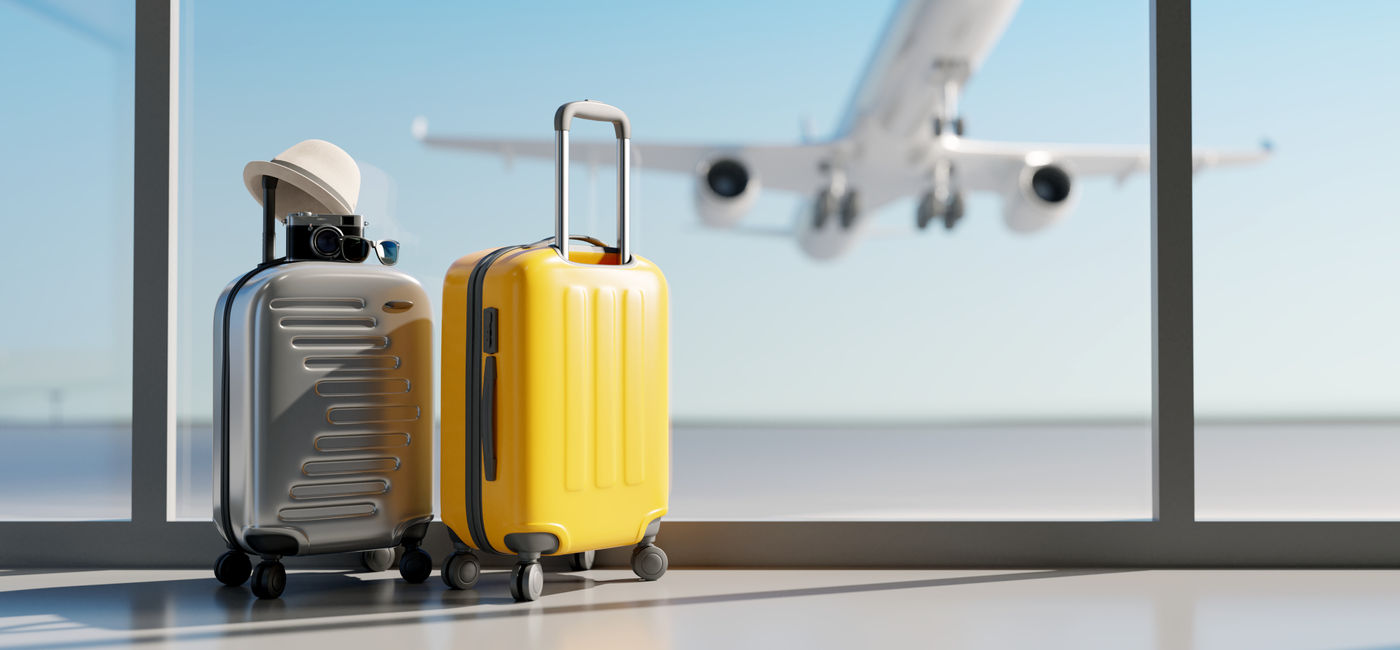 Image: Luggage sitting at the airport with a plane taking off in the background. (Photo Credit: Adobe Stock/aanbetta)