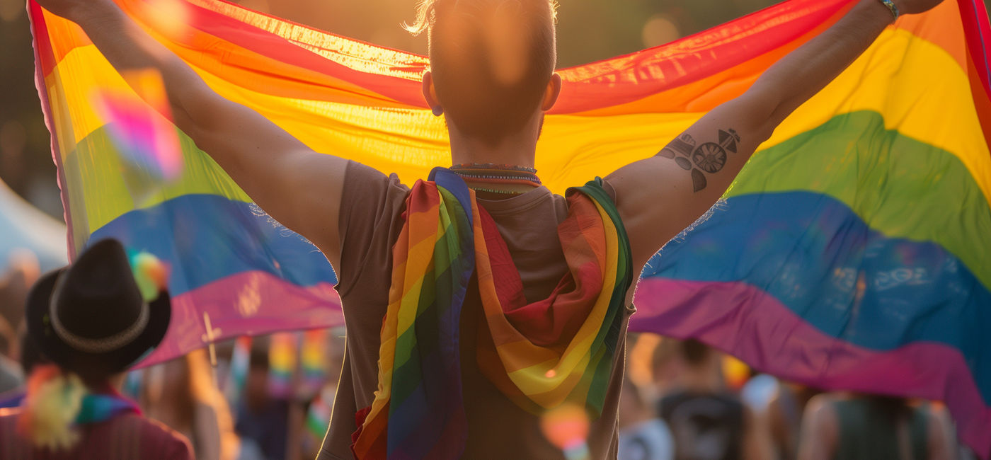 Image: Person holding an LGBTQ+ Pride flag. (Photo Credit: Adobe Stock/Vasilina FC)