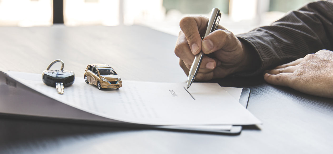 Image: Traveler signing a rental car agreement. (Photo Credit: Puwasit Inyavileart/Adobe)