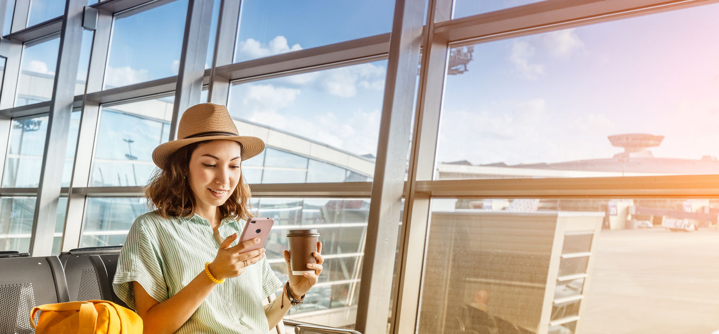 Image: Traveler using her phone at the airport. (Photo Credit: EdNurg/Adobe)