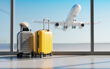 Luggage sitting at the airport with a plane taking off in the background.