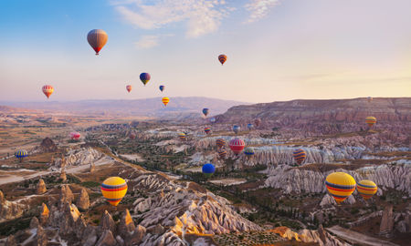 Hot air balloon flying over rock landscape at Cappadocia Turkey (photo via TPopova / iStock / Getty Images Plus)