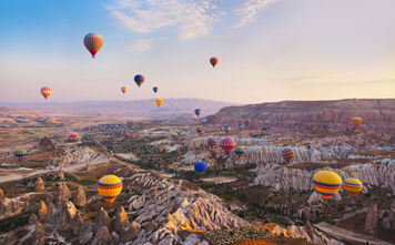 Hot air balloon flying over rock landscape at Cappadocia Turkey (photo via TPopova / iStock / Getty Images Plus)