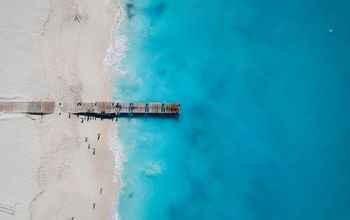 Drone photo of pier in Grace Bay, Providenciales, Turks and Caicos. The caribbean blue sea and white sandy beaches can be seen (photo via JoaoBarcelos / iStock / Getty Images Plus)