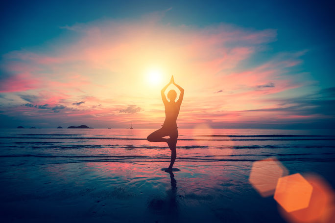 Woman doing yoga on the beach at sunset.